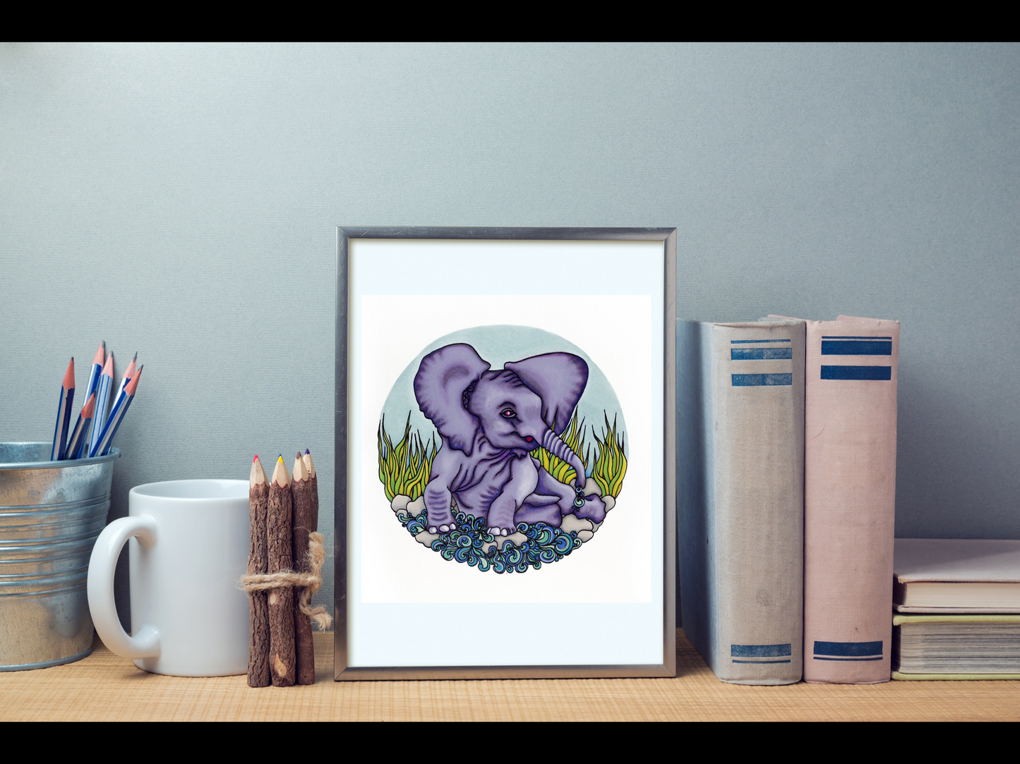 The Elephants Bath illustration framed in a small frame on the top of a bookshelf. The setting of this photo is perfect with the colours of the illustration.