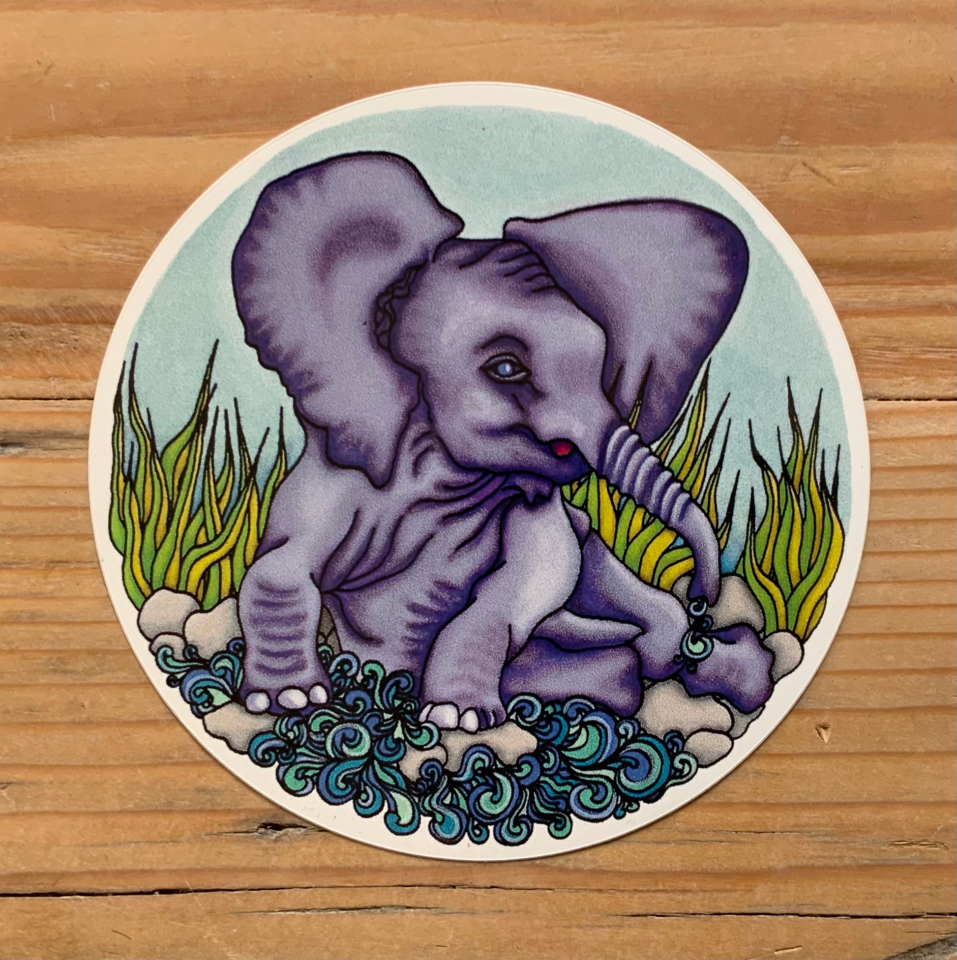 A close up of the baby African Elephant sticker available in the sticker section of my shop. Purple elephant playing and washing in a river with grass behind him.