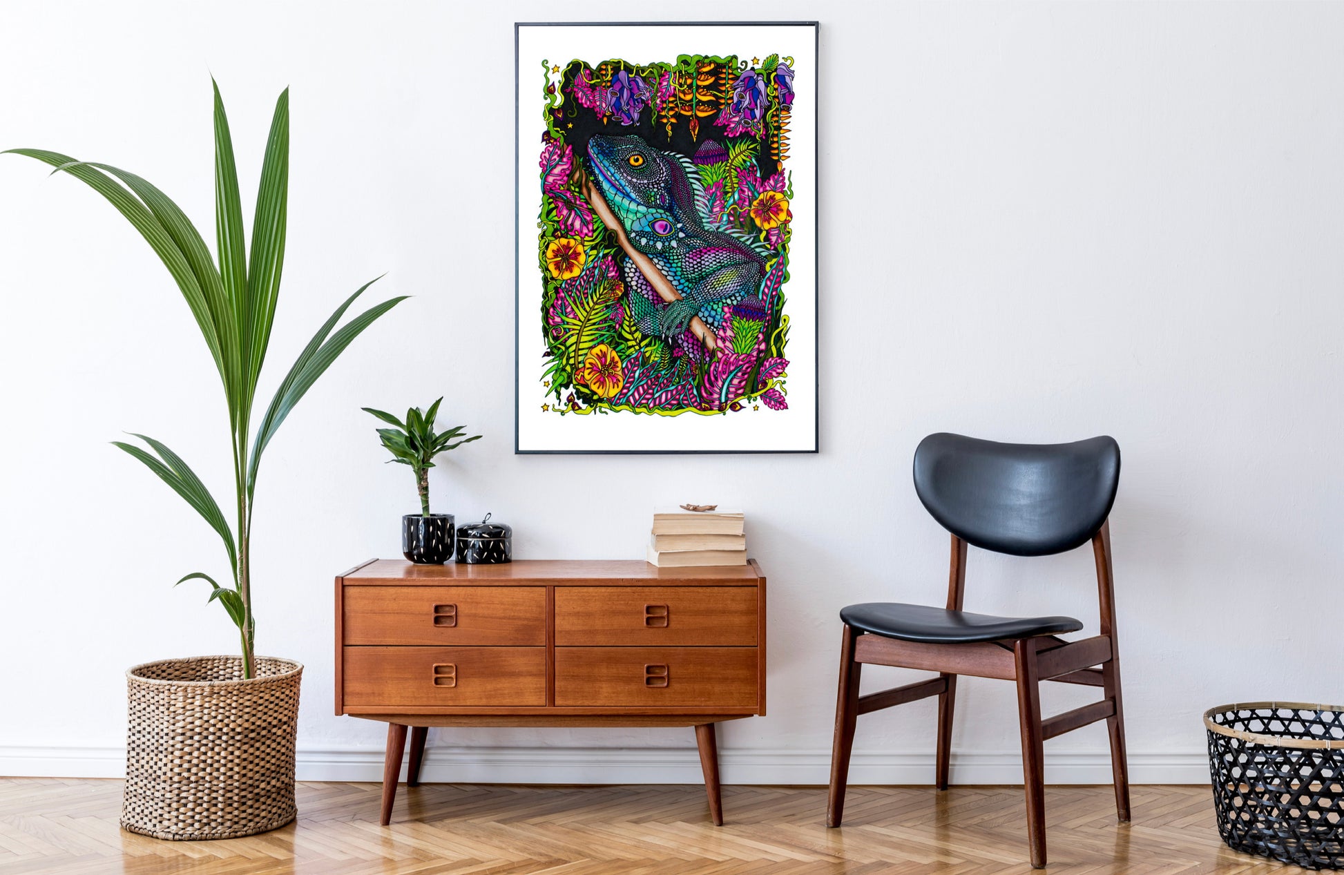 Iguana print in A1 large size on a white wall. Around the picture is a couple of plants, one large one small. A sideboard with some books and a tin on top and a vintage Scandinavian chair. The floor is made of wood and there is a black basket just hanging out of the frame.